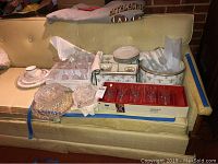 Crystal and glass dishes arranged on a yellow couch, showing various glass dessert dishes, some crystal, and more items in boxes.