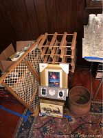 Wooden baby gate leaning against wooden wall, two wooden wine racks, framed print, glassware partially visible on the side, rustic bucket on the floor.