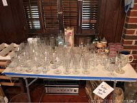 Table full of assorted glassware including water glasses, coupe, hurricane, flute, pilsner, dessert bowls and Irish coffee mugs. Some glasses look dirty.