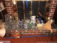 Glass vases, bowls, ashtrays, fireplace tools arranged on and in front of fireplace with brass screen