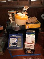 Overall photo showing multiple kitchen appliances and tools including taco racks, salad spinner, cheese keeper, can opener, and grinder boxes.