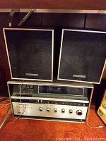 Full view of Panasonic stereo system with two speakers on top placed on a wooden surface.
