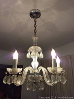 Front view of clear crystal chandelier with five candle bulbs and hanging crystal droplets, mounted on ceiling chain with metal ceiling plate.