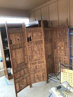 Four-panel carved wooden screen standing unfolded indoors, showing intricate carved designs and partial damage.