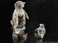 Photo of large and small Swarovski crystal penguin figurines on a reflective black surface showing faceted detail.