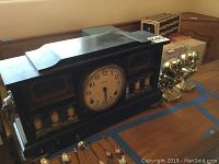 Full shot of the Ingraham slate mantel clock and brass thinking man bookends on a table, showing overall size and condition.