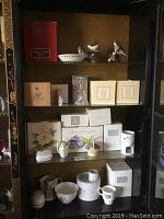 Cabinet shelf displaying multiple Avon collectible items: bird figurines, ceramic vessels, and boxes