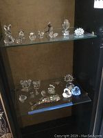 Two glass shelves with multiple clear crystal animal figurines and heart shapes
