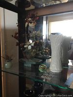 Photo of shelf showing all items: Lenox vase on the right, mixed media flower decor behind, apple and small cup in front.