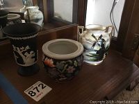 Photo of three vases: black vase with white relief figures, colorful floral vase, and white vase with windmill painting.