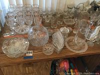 Overview of cut crystal items arranged on wooden surface, including stemware, bowls, covered jar, candle holders, and smaller dishes.