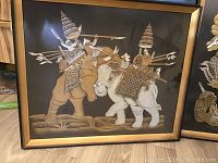 Framed oriental themed print showing two figures on elephants with spears.