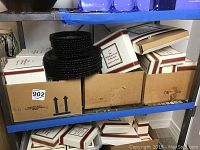 Four cardboard boxes on lower shelf labeled “Cape Cod” containing boxed glassware; stack of nine black glass berry bowls atop boxes