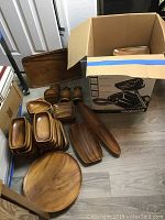 Various wooden trays, bowls, and specialty shaped pieces including pineapple and dolphin, placed on floor and partially in box.