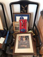 Framed color portrait of Brigadier General Robert W Waltz on wooden chair with framed memorabilia and binoculars.