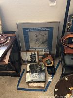 Layout of framed poster, books including 'One Box', smaller framed photos, plaque with insignia, and leather binocular case arranged on floor.
