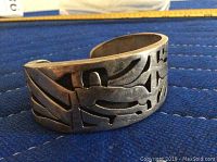 Cuff bracelet front view displaying cut-out tribal pattern.
