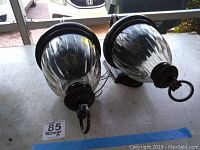 Pair of outdoor wall sconces on tabletop, showing ribbed glass globes and dark bronze metal mounting brackets and arms.