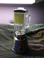 Full view of Osterizer Beehive Art Deco blender with glass pitcher and lid, plugged in and placed on a blanket with a purple wall background.