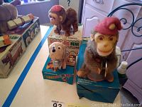 Three vintage wind-up toys displayed with their original boxes, showing a mischievous monkey, a cheerful puppy, and a cymbal monkey.