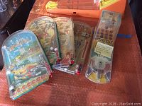 Five vintage plastic Bagatelle marble pinball games arranged showing various colorful playfields and artwork