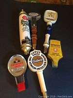 Photo showing seven vintage German beer tap handles laid flat, displaying logos and design details including Pilsner Urquell, Lowenbrau, Warsteiner, Spaten Munich, and Dortmunder Union.