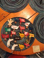 Top view of 18 assorted bottle top pourers arranged circularly on a woven mat, featuring brand logos like Calvert, White Label, PM, Philadelphia and others.