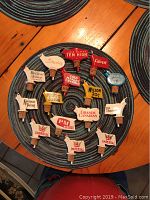 Top-down view of 15 vintage branded bottle top pourers arranged on a circular placemat, brands visible including Imperial, Kentucky Tavern, Calvert, Wilson, and others.
