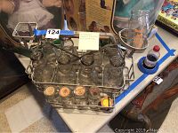 Full view of Kilgerman metal milk carrier holding eight vintage glass milk jars with screw-on metal lids, showing carrier handle and jar arrangement.