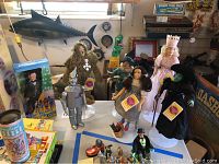 Photo showing seven 12-inch Wizard of Oz fiftieth anniversary dolls posed on a table with stands, including The Wizard, Dorothy, Tin Man, Scarecrow, The Lion, The Good Witch, and The Bad Witch.