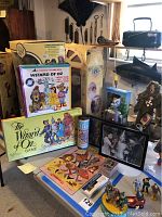 Photo showing multiple Wizard of Oz themed collectibles including boxed board game, figurines, black and white photo, and other small items