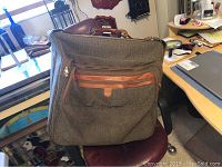 Exterior view of large brown fabric suitcase with brown leather zipper accents and handle.