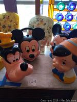 Front view of three Disney character banks: Goofy, Mickey Mouse, Pinocchio on marble surface