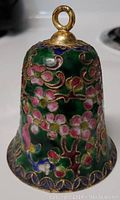 Side view of the cloisonne bell showing detailed floral cloisonne enamel on green background with gold accents and a hanging loop on top.