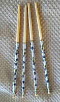 Four vintage cloisonne enamel chopsticks with floral designs and gold accents on a textured cloth background.
