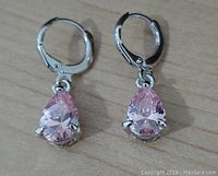 Front view of the pair of pear-shaped pink topaz dangle earrings with hinged hoop clasps on a wooden surface.