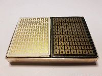 Two decks of vintage Playboy playing cards with gold Playboy bunny logo patterned backs, one white and one black.