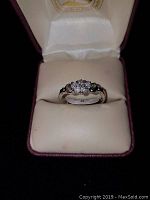 Ring inside padded jewelry box showing front of clear stone ring in silver-colored setting.