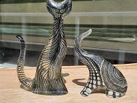 Two black and white patterned acrylic animal figurines: a tall cat and a shorter elephant on a wooden surface, photographed outdoors with reflections seen in background windows.