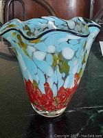 Front perspective of multicoloured glass vase with wavy rim showing light blue, white, and red patterns.