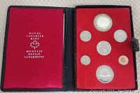 Photo of open black case and inner red felt insert holding seven Canadian proof coins including a large silver dollar with Mountie design.