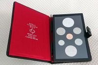 Open black clamshell case with red interior showing seven proof coins in black holder.