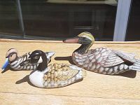 Front and side view of three hand-carved wooden duck decoys arranged on a wooden surface in sunlight.
