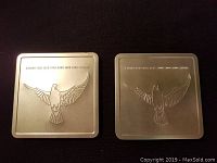 Two silver square coins each embossed with a flying dove and year markings for 1999 and 2000, displayed side by side.