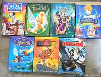 Seven Disney and DreamWorks children's DVDs arranged in two rows, showing front covers including 101 Dalmatians II, Tinker Bell, Tangled, Cinderella II, The Rescuers, Lion King 1½, and How to Train Your Dragon.