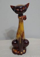 Front view of Blue Mountain Pottery cat figurine showing the tall neck, brown and amber drip glaze, whimsical facial features, and seated posture.