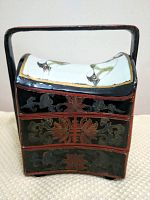 Front view of the decorative storage box showing the bird painted curved lid, black lacquer with gold and red floral patterns, and integrated handle.