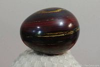 Photo of dark red polished stone egg showing yellow and black streak patterns on one side.