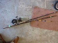 Photo showing two fishing rods lying crossed on a garage floor with signs of wear and some tape on rods.