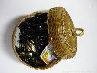 Top-down photo of small round woven basket with lid open revealing costume jewelry inside.